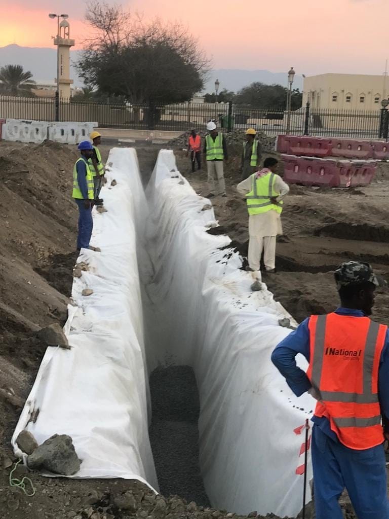 Workers placing geotextile in a trench for a cut-off wall